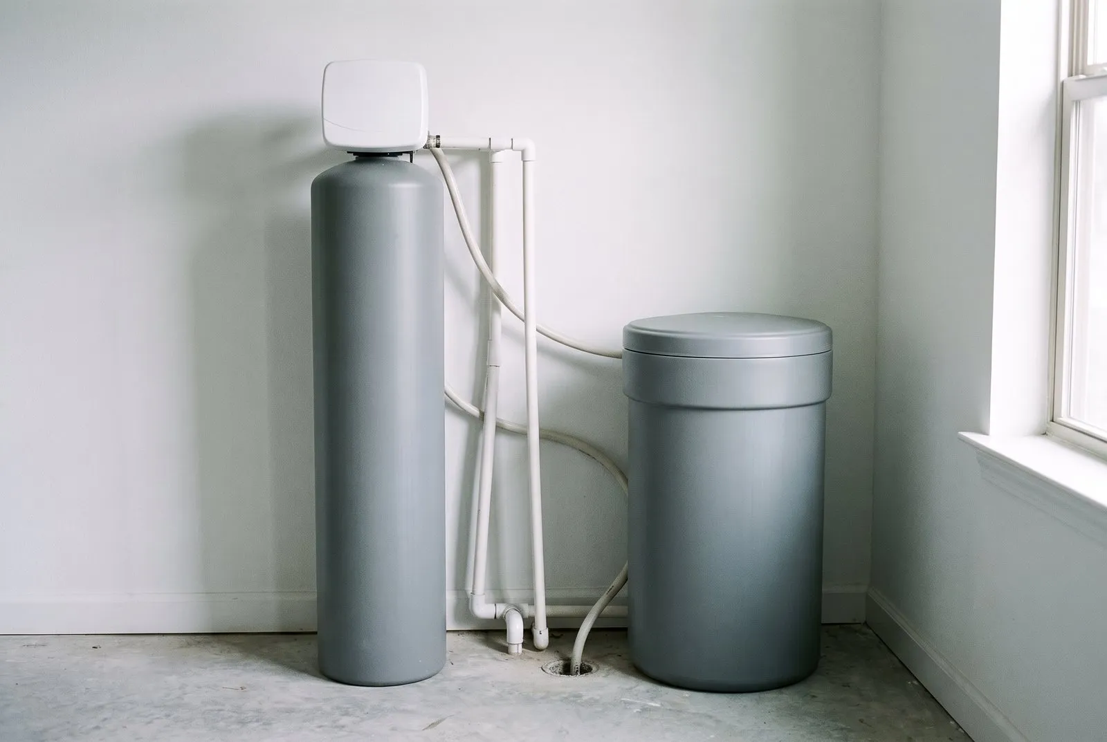 A water softener tank and a brine tank standing side by side in a utility room, with no brand markings.